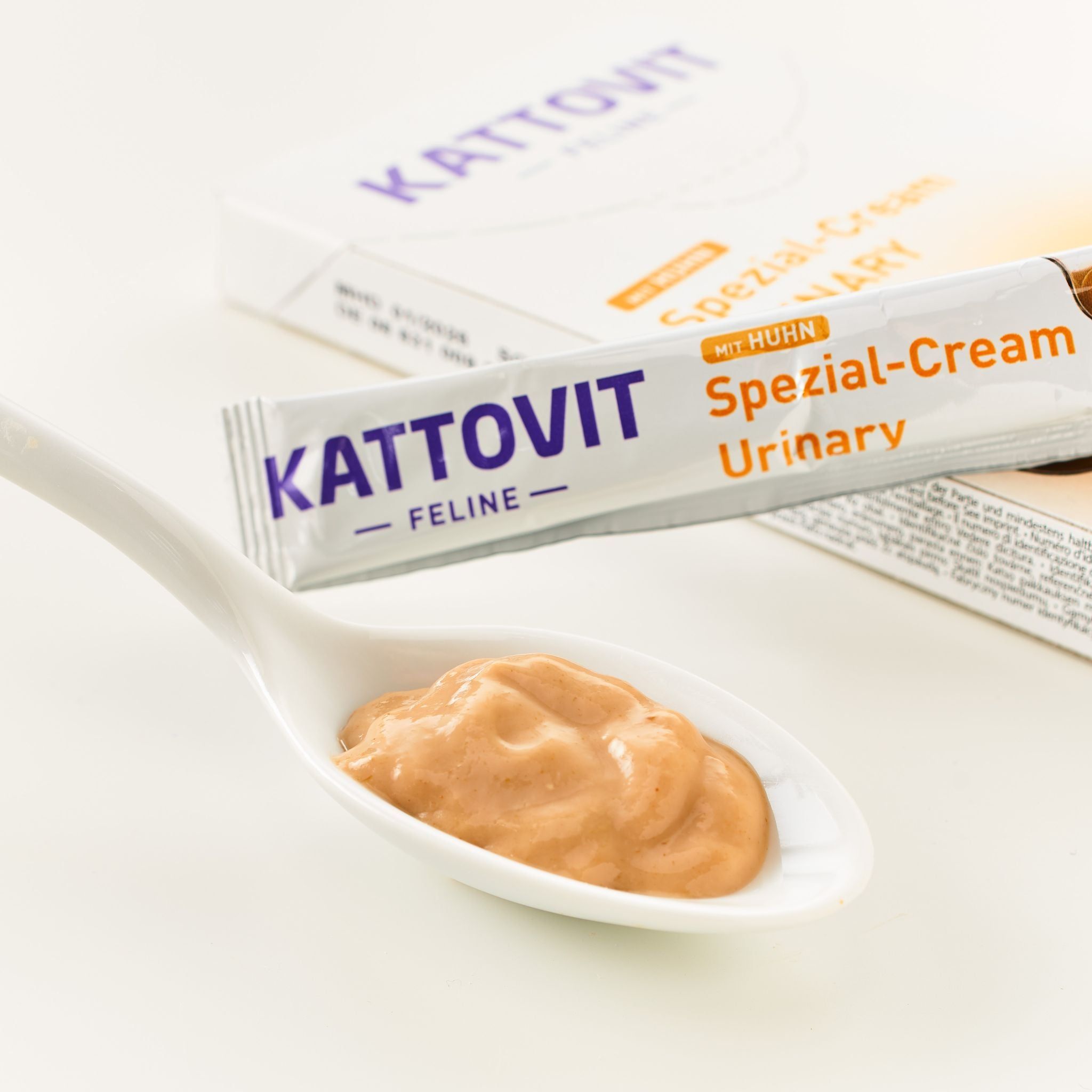 Cucchiaio con sostanza cremosa. Tubo KATTOVIT Urinary Spezial-Cream e scatola sullo sfondo. Nome del prodotto ben visibile sul tubo.