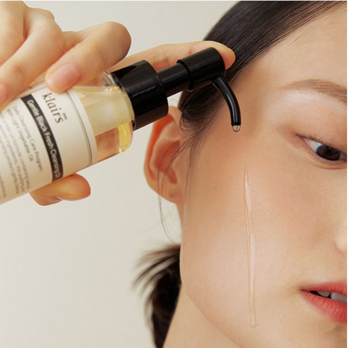 Persona che tiene in mano un flacone di Gentle Black Fresh Cleansing Oil. L'olio viene applicato sulla pelle. Primo piano del viso.