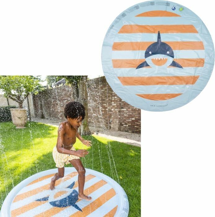 Bambino in pantaloncini a righe gialle corre su tappeto rotondo con motivo squalo. Spruzzi d'acqua.