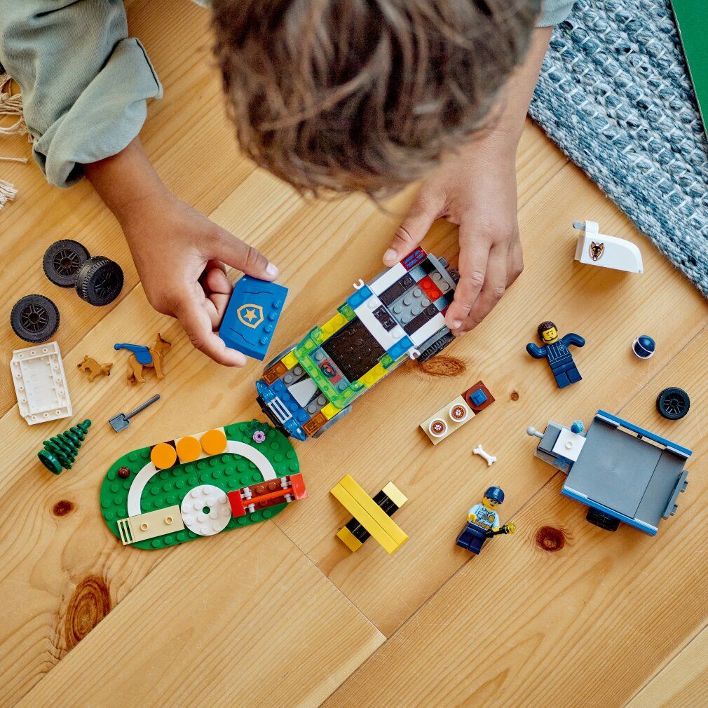 Set LEGO City. Pezzi su pavimento in legno. SUV, personaggi, cani, percorso. Parti da assemblare.