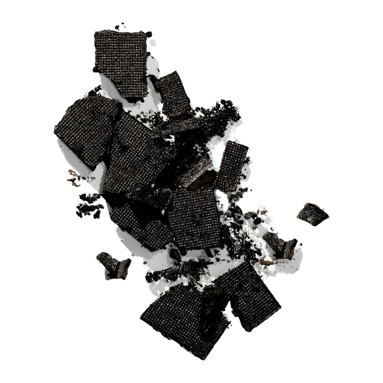 Pezzi di prodotto Color Wow Root Cover Up neri schiacciati. Mostrato su sfondo bianco. Diverse forme e dimensioni.