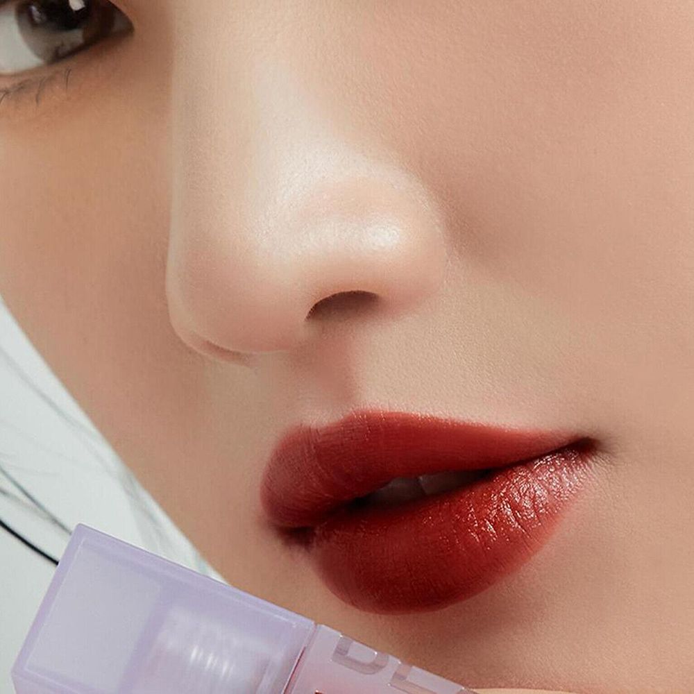 Primo piano di labbra coperte da un lucidalabbra rosso-marrone. La bocca è leggermente aperta.