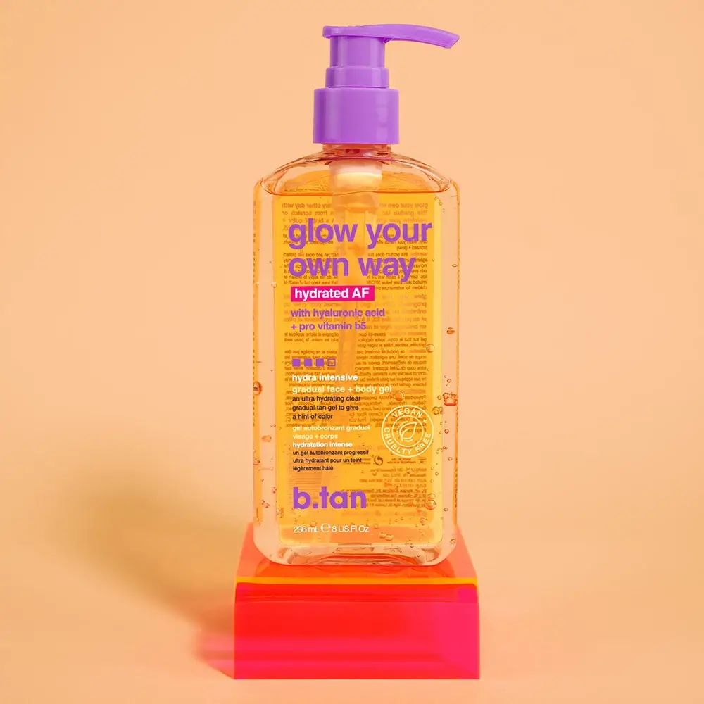Flacone trasparente con pompa viola. Scritta "glow your own way hydrated AF". Sigillo vegano. Su sfondo rosso e arancione.
