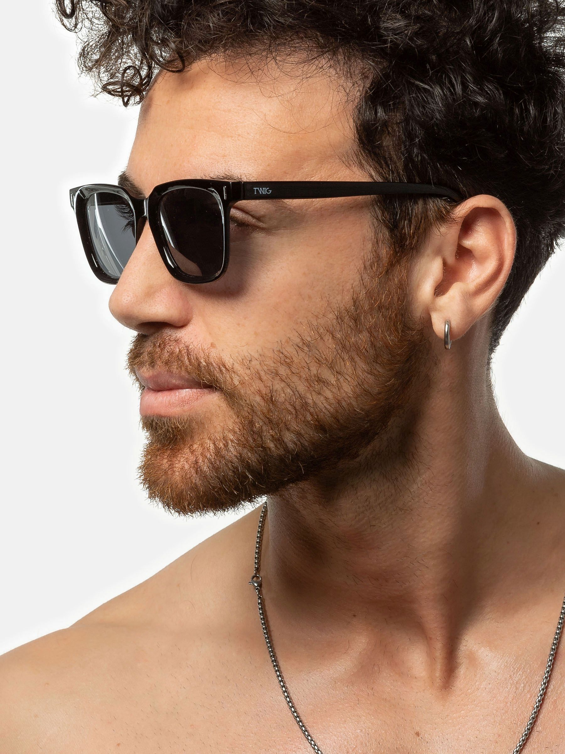 Uomo con occhiali da sole Twig. Montatura nera, lenti rettangolari. Vista laterale.