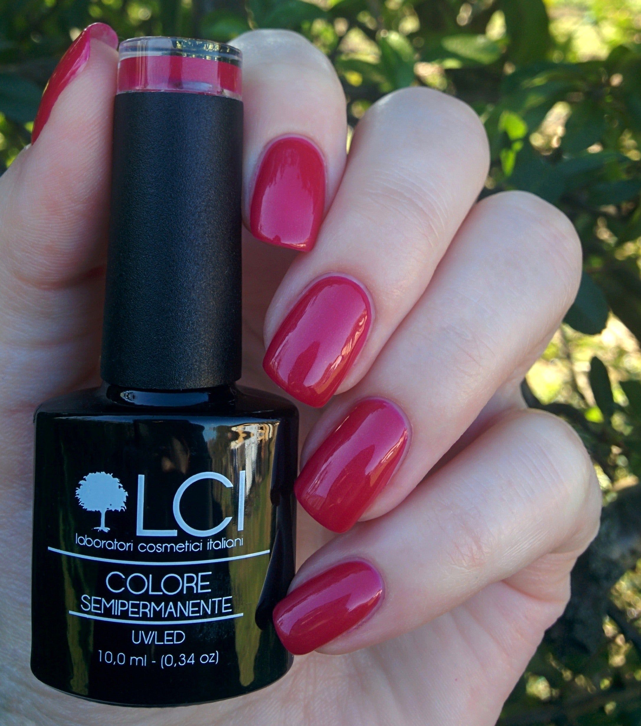 Flacone di smalto e unghie laccate rosso ciliegia. Flacone nero con etichetta, mano con unghie laccate.