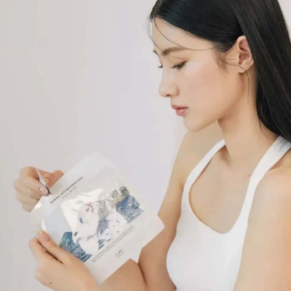 Donna tiene la confezione della maschera viso. Busta bianca con immagine paesaggio. Marchio: Dr. Althea.