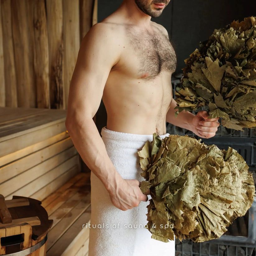 Uomo che tiene due fasci di betulla. Indossa un asciugamano. Testo: Rituals of sauna & spa.