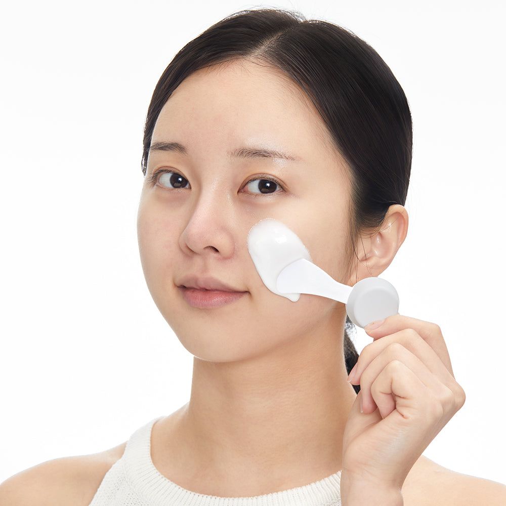 Una donna applica una maschera facciale con un applicatore.