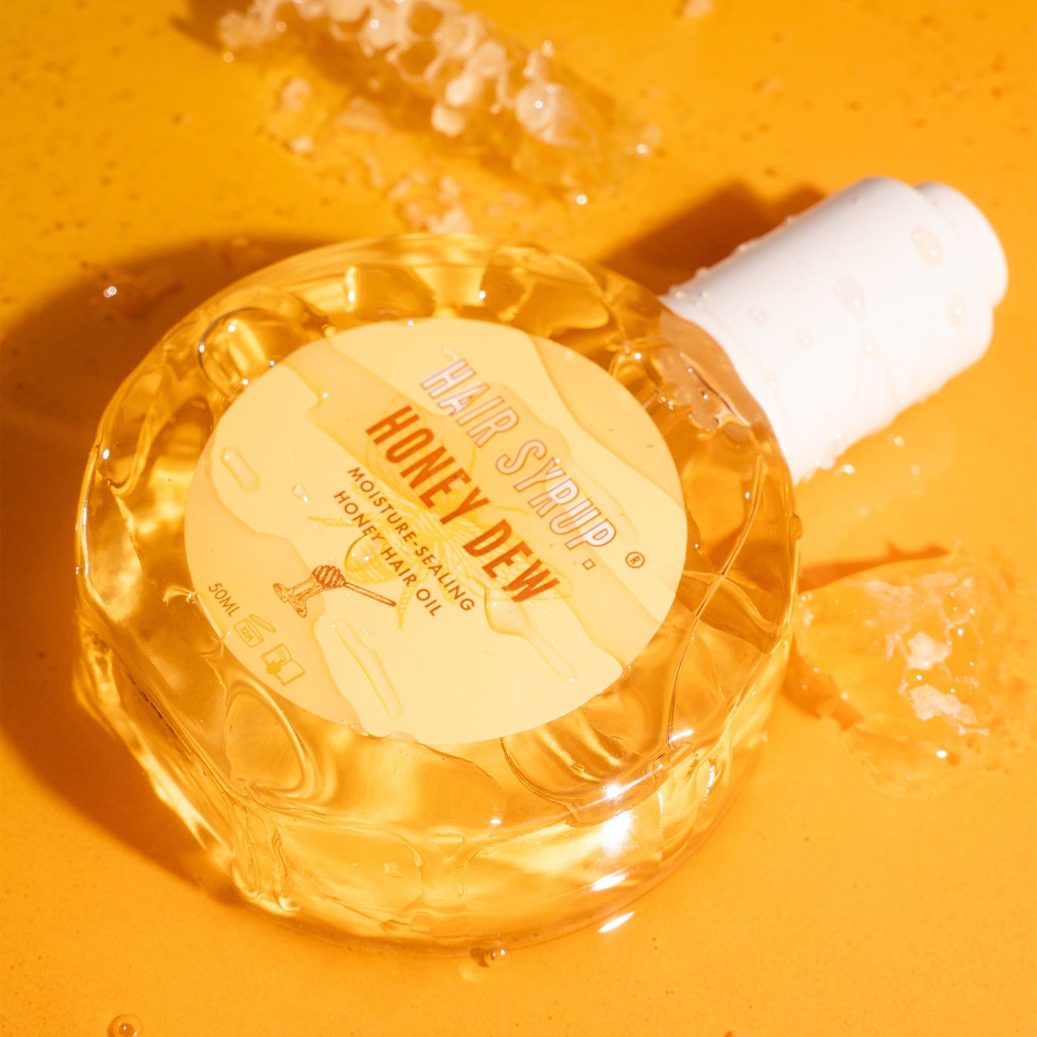 Flacone rotondo in vetro con tappo bianco. Etichetta con testo. Flacone appoggiato su sfondo giallo. Favi sullo sfondo.