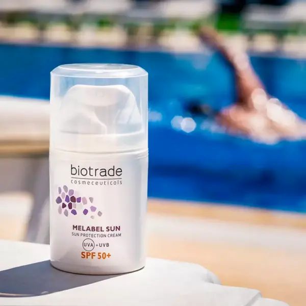 Flacone bianco Biotrade Melabel Sun SPF 50. Scritta: Melabel Sun, SPF 50+. Sullo sfondo, un nuotatore in piscina.