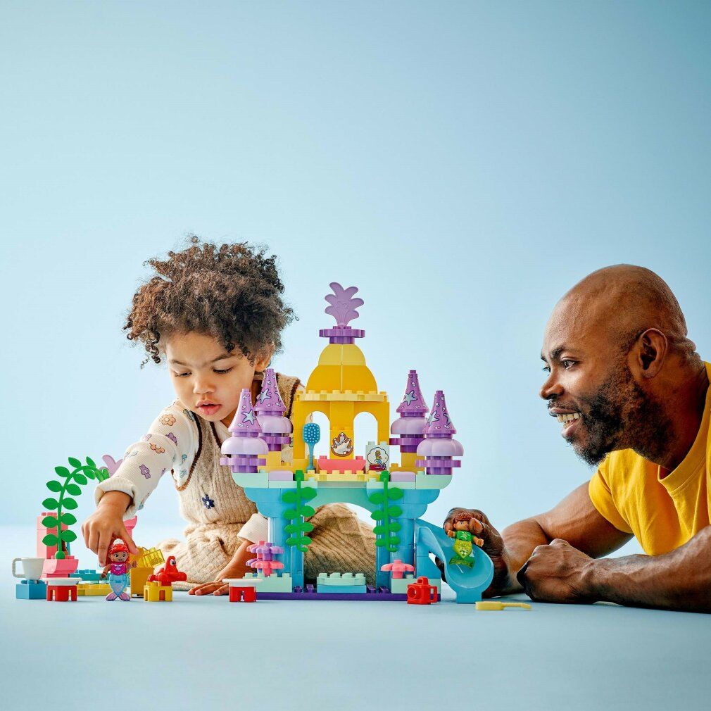 Bambino gioca con il set LEGO Duplo. Il magico palazzo sottomarino di Ariel. Castello, personaggi, accessori. Adulto osserva.