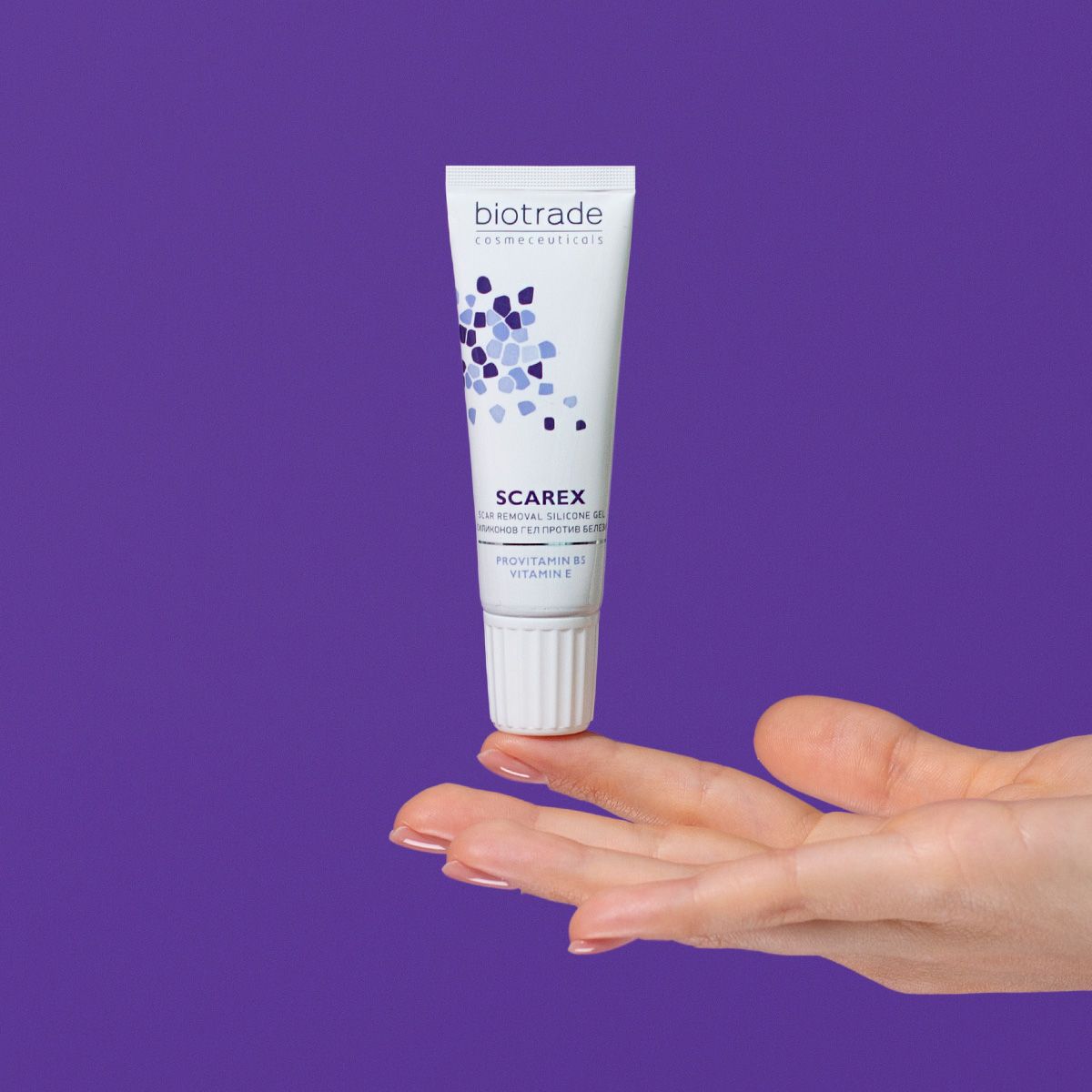 Tubo bianco-blu con nome del prodotto e logo, tenuto in mano, su sfondo viola.