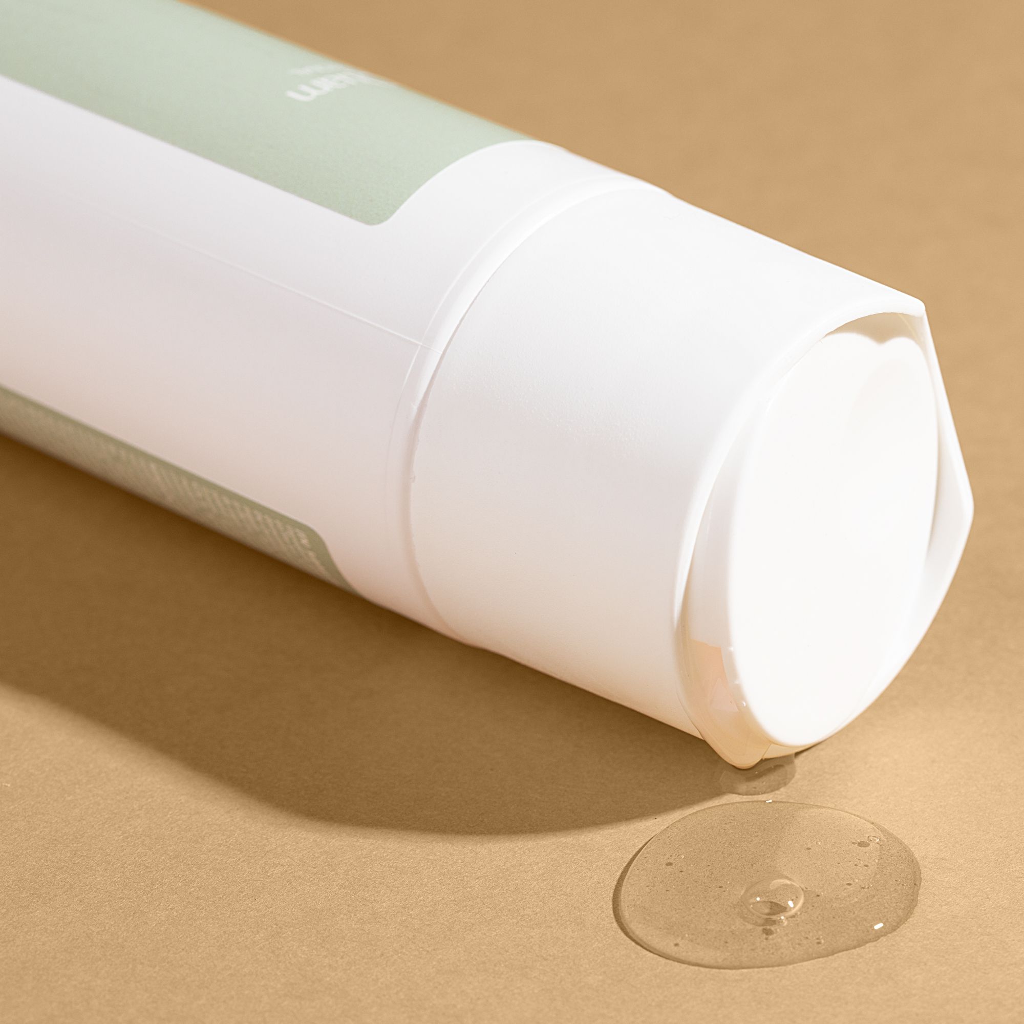 Testa di flacone di shampoo bianco con liquido trasparente che fuoriesce su sfondo marrone.