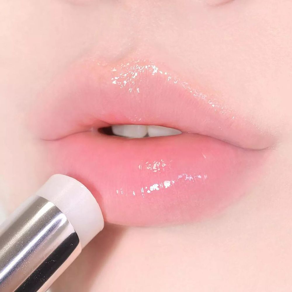 Labbra con balsamo applicato. Il balsamo è in uno stick d'argento. Le labbra sono lucide e rosa.