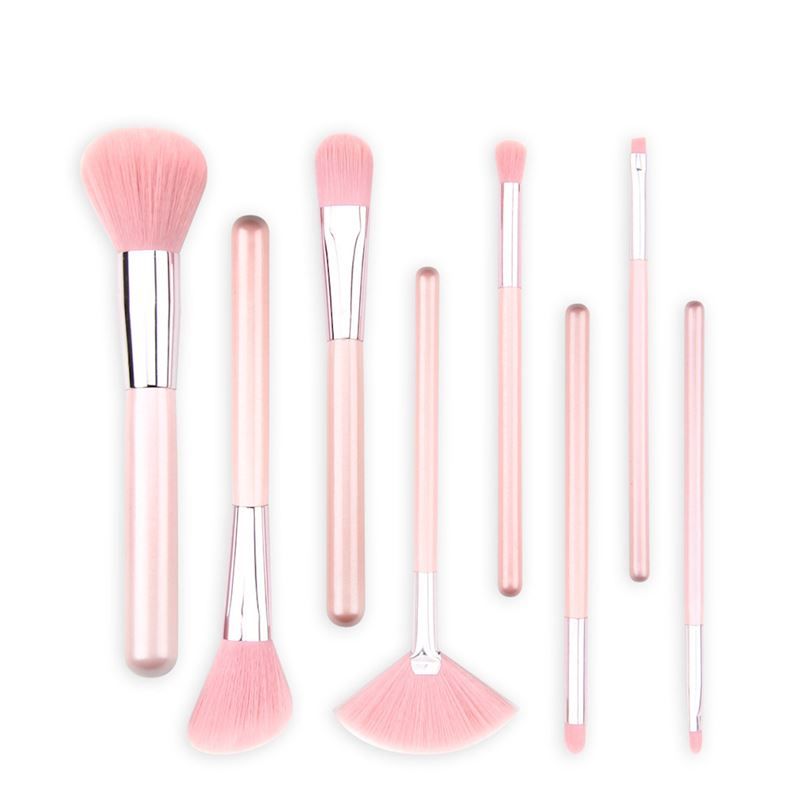 Un set di otto pennelli per il trucco rosa con accenti argentati, su sfondo bianco.