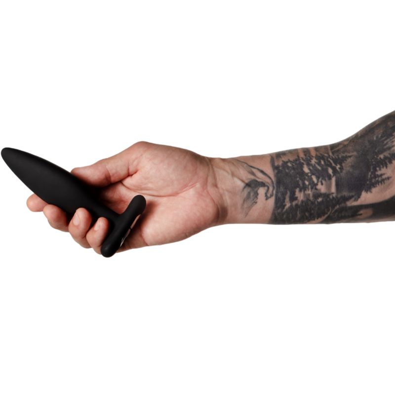 Plug anale nero in una mano. Braccio tatuato. Fusto conico con impugnatura a T.