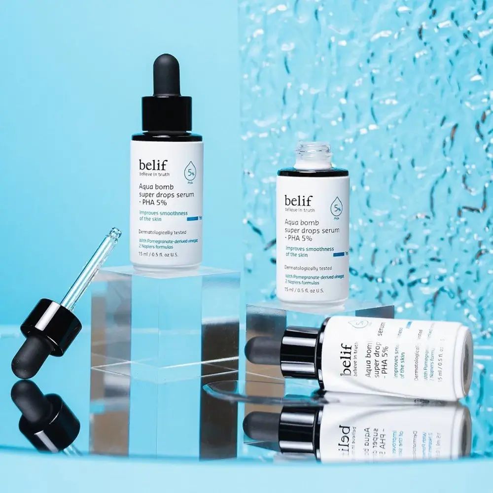 Diversi flaconi di siero con pipette nere. Nome del prodotto e ingredienti sulle etichette. Alcuni flaconi sono posizionati su una superficie.