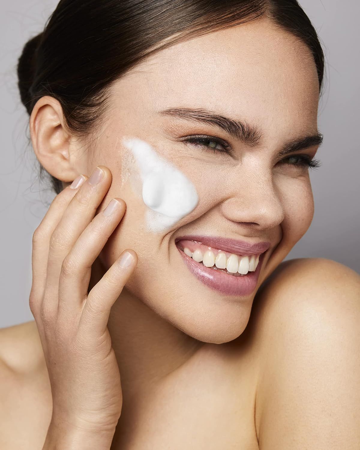 Donna con schiuma sulla guancia, sorridente. Sfondo: sfondo grigio. La schiuma è bianca.