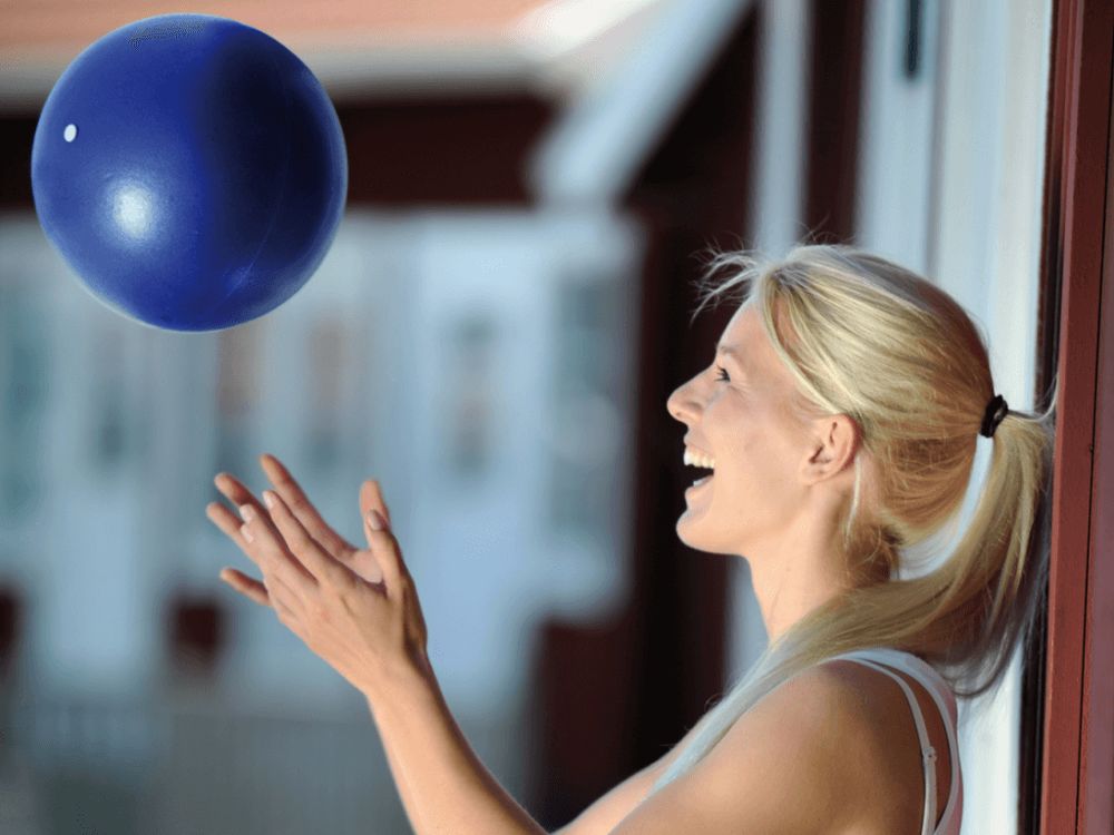 Donna lancia palla blu in aria. Sfondo: casa, finestra.