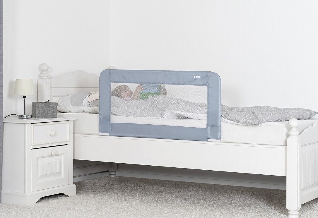 Barriera letto blu montata. Bambino nel letto. Letto bianco, comodino con lampada.