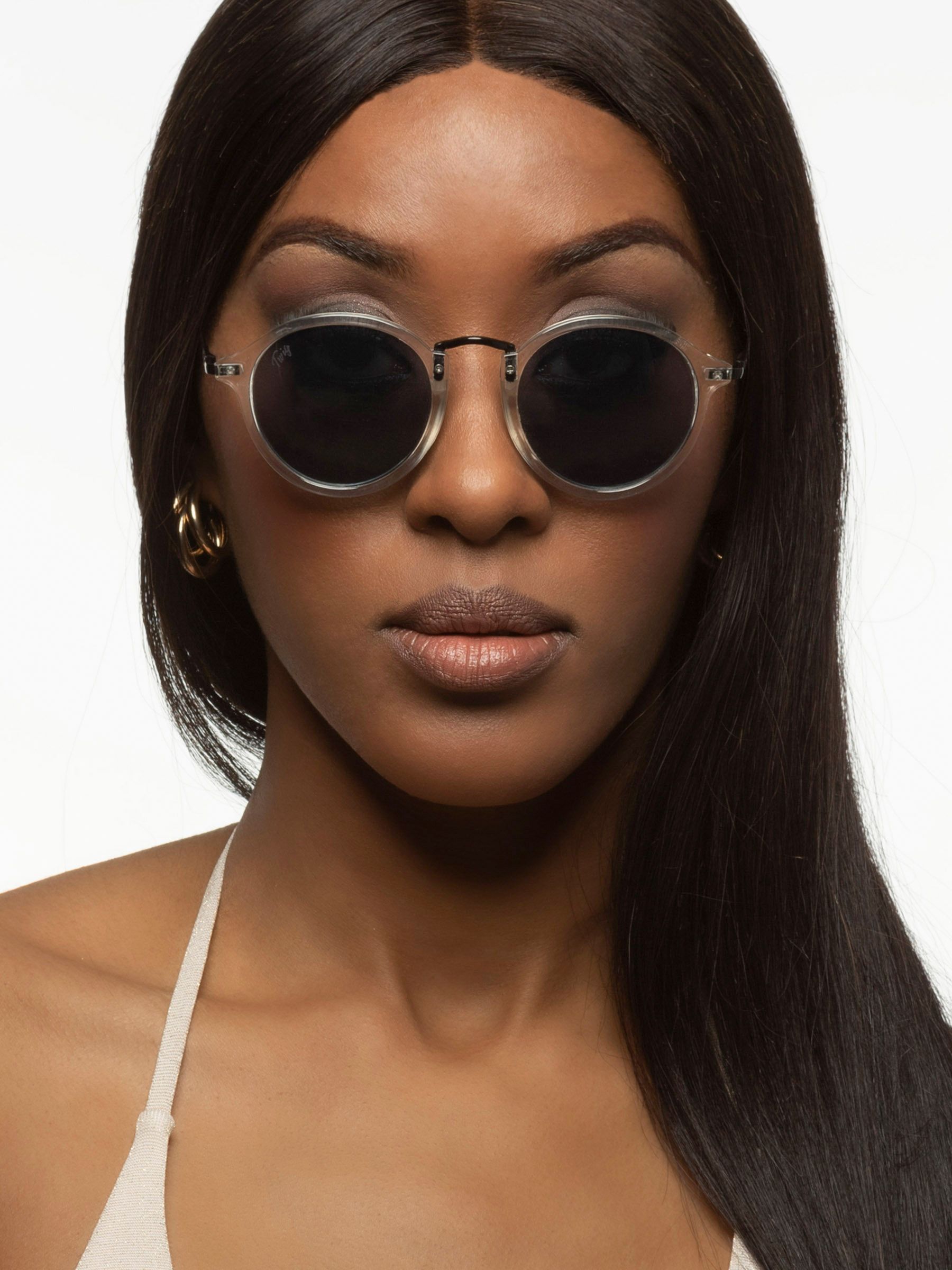 Donna con occhiali da sole rotondi con montatura trasparente e lenti scure. Aste nere.