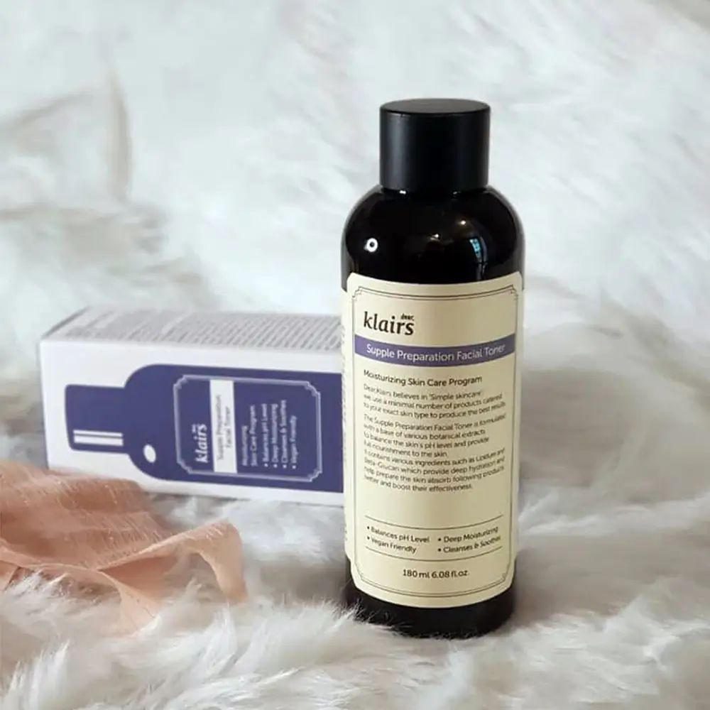 Flacone di toner viso Klairs. Flacone marrone con tappo nero. Etichetta con informazioni sul prodotto. Sfondo: tessuto.