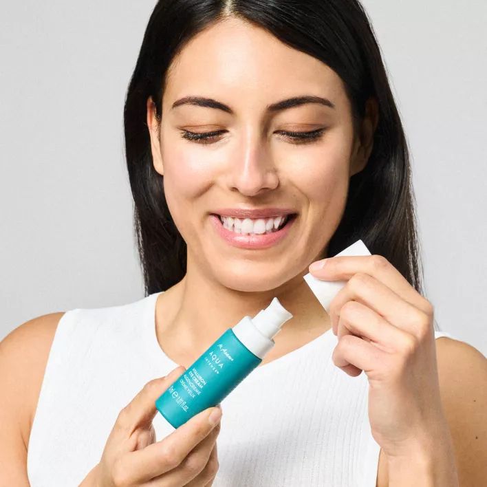 Donna che apre un flacone turchese. Scritta: M. Asam AQUA INTENSE Hyaluron Eye Cream.