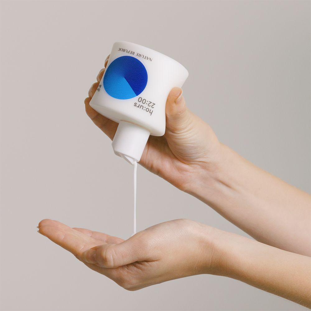 Flacone bianco, cerchio blu. Scritta: ho:urs 22:00, NATURE REPUBLIC. Lozione versata nella mano.