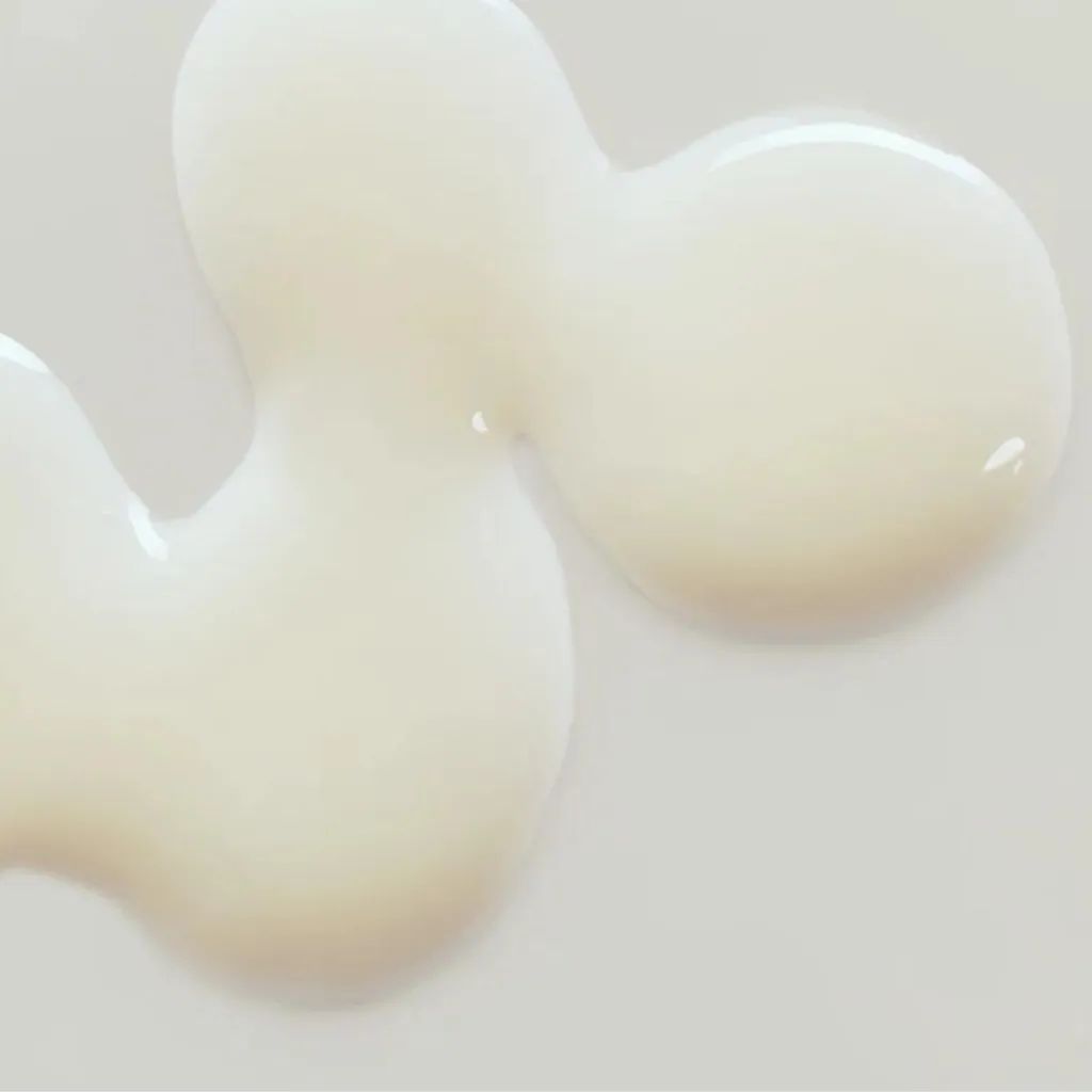 Primo piano di siero su sfondo bianco. Gocce di siero color crema di forma irregolare. Superficie liscia e lucida.