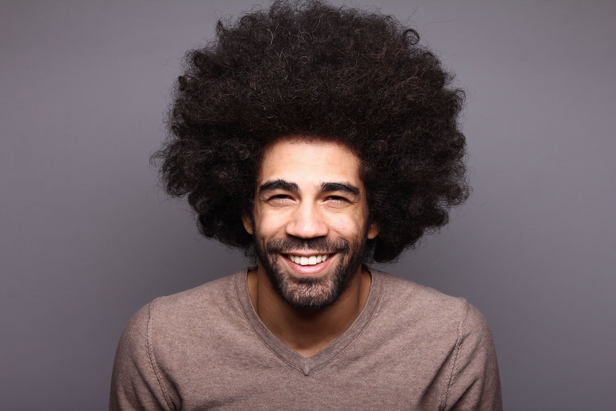 Uomo con capelli afro voluminosi sorride alla fotocamera.