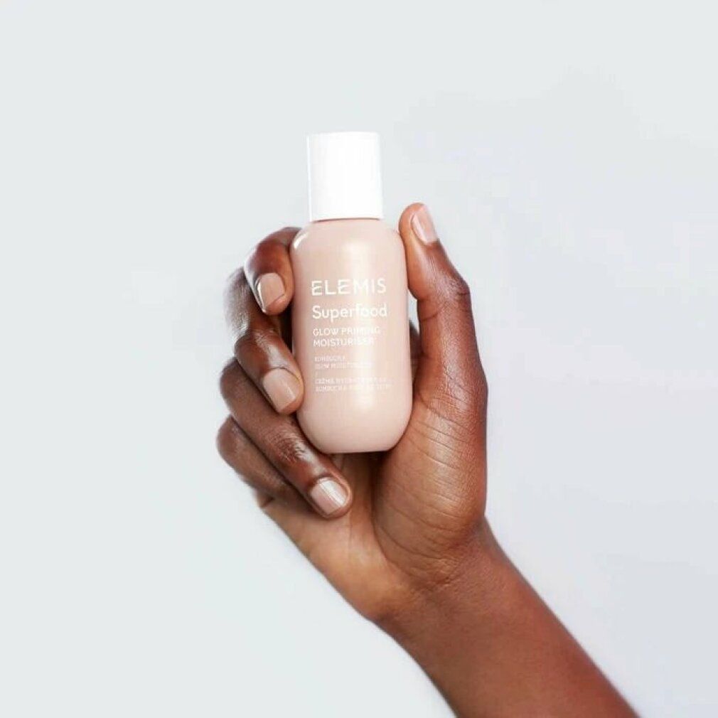 Mano che tiene una bottiglia di Elemis Superfood Glow Priming Moisturiser. Tappo bianco, bottiglia rosa, nome del prodotto visibile.