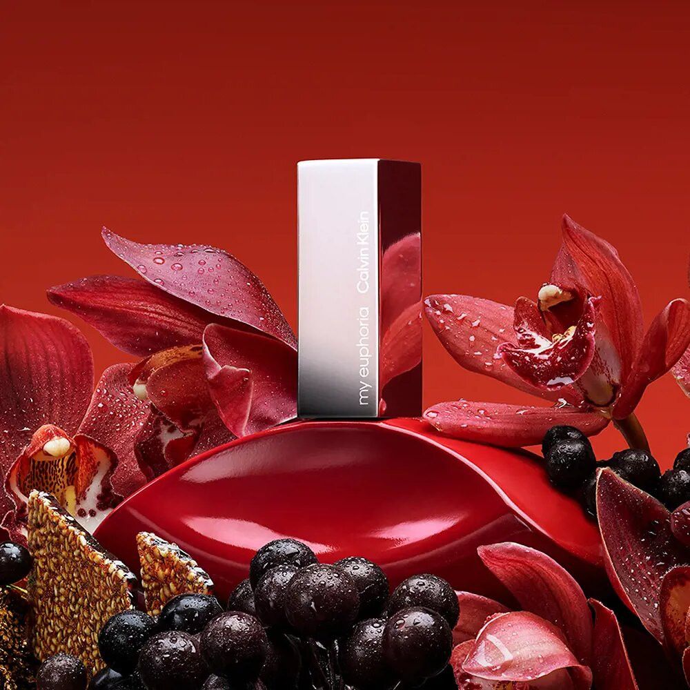 Flacone rosso con tappo argentato, circondato da fiori rossi e bacche scure. Scritta "my euphoria" e "Calvin Klein".