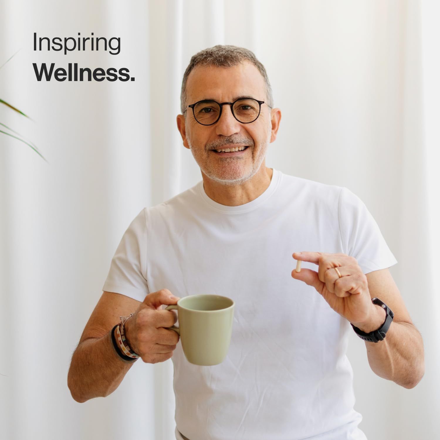 Uomo con occhiali tiene una capsula e una tazza. Indossa una maglietta bianca. Scritta: Inspiring Wellness.