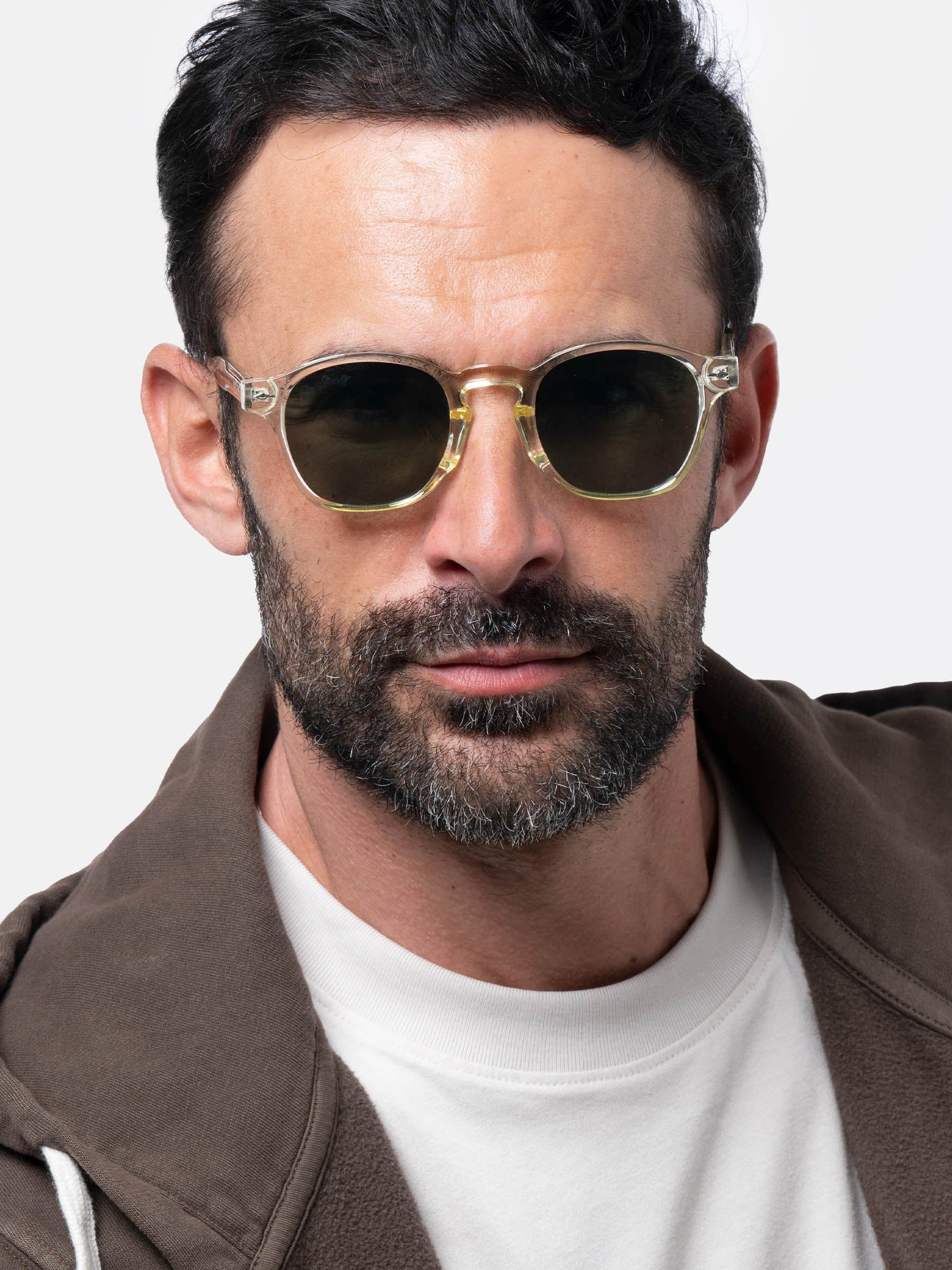 Uomo con occhiali da sole con montatura trasparente e lenti verdi. Il logo Herling non è visibile.