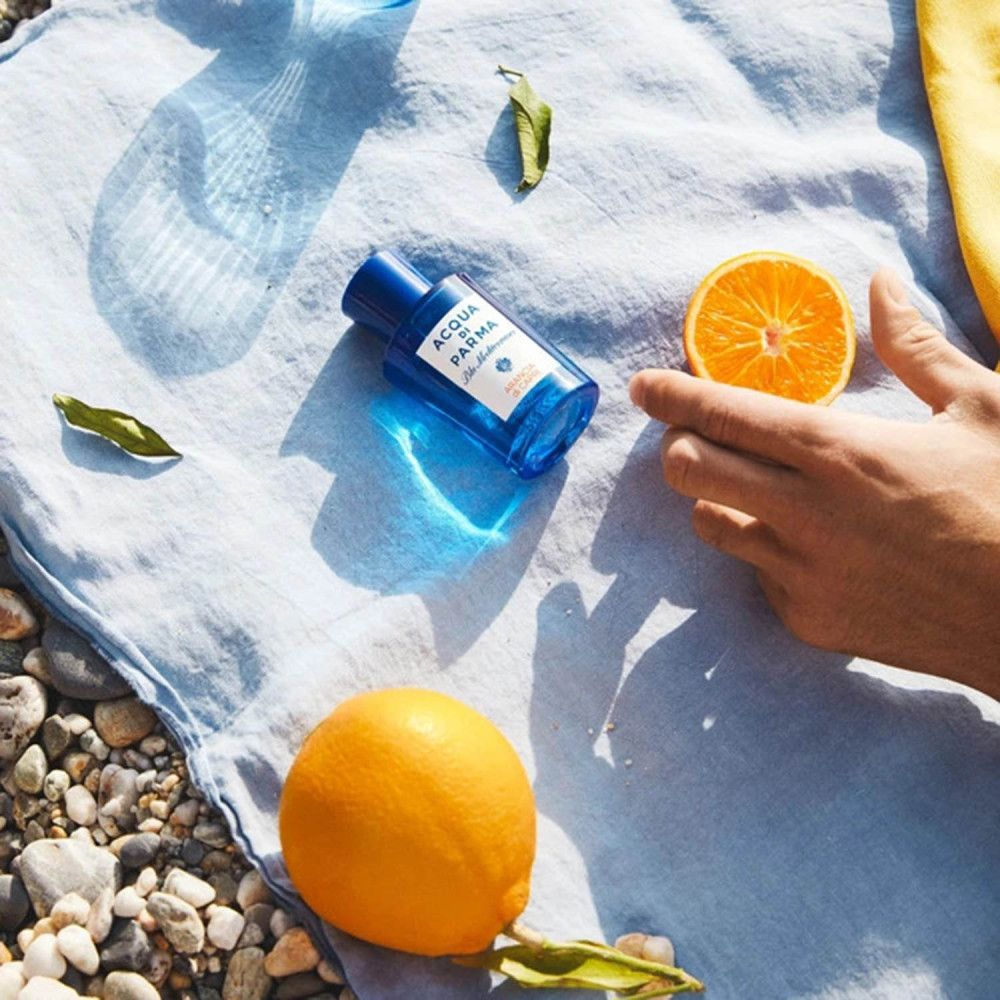 Flacone di profumo blu, arance e foglie su tessuto blu. Scritta: ACQUA DI PARMA, Blu Mediterraneo, Arancia di Capri.