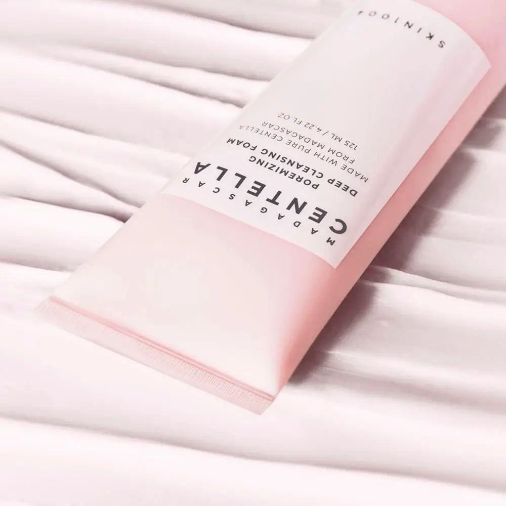 Primo piano di una sezione di tubo rosa. Testo: MADAGASCAR CENTELLA, Poremizing Deep Cleansing Foam. Marchio SKIN1004.