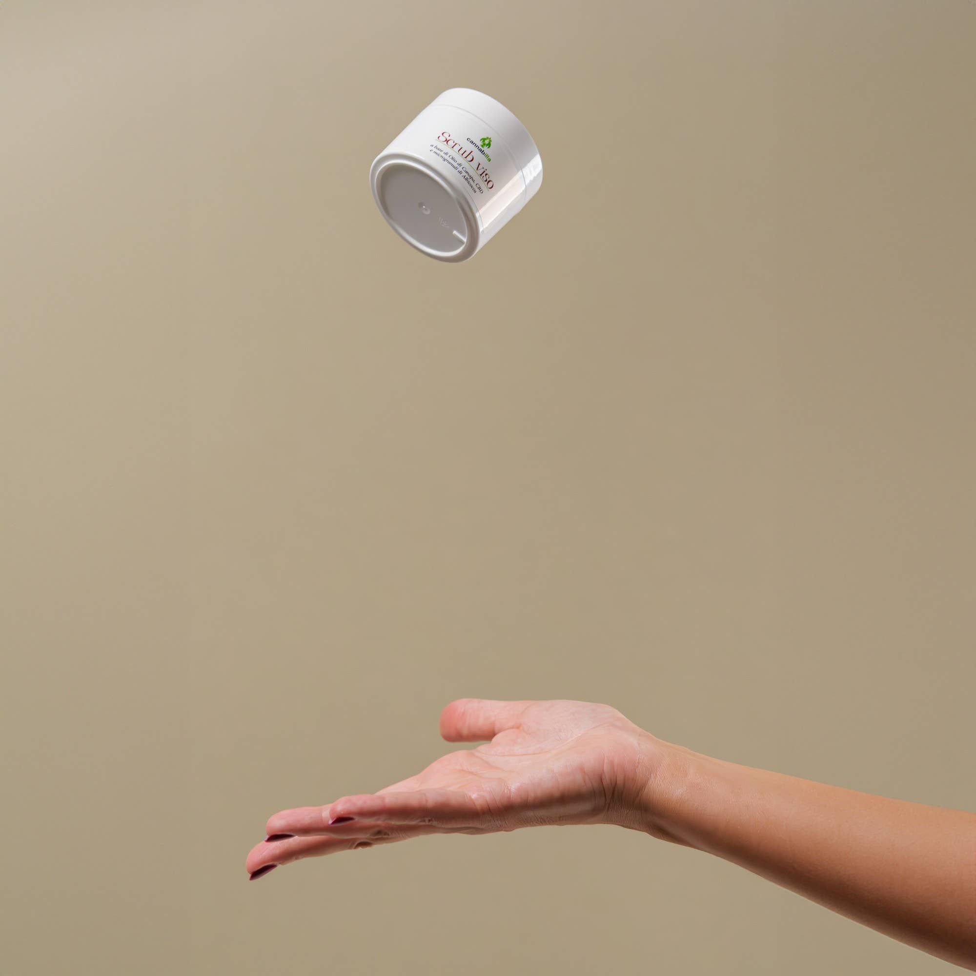 Vaso bianco "Scrub viso" in aria, sopra una mano. Logo "cannabilla" visibile.