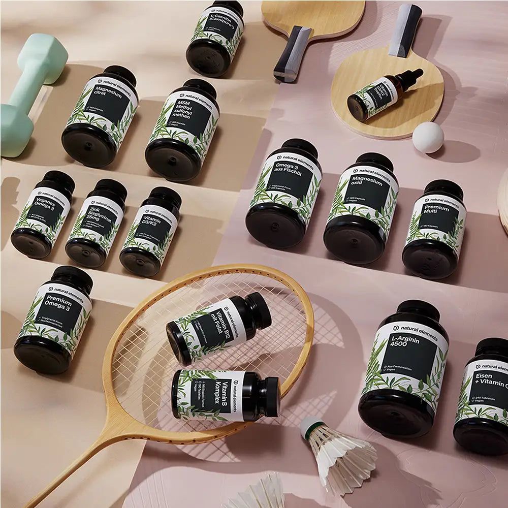 Diversi barattoli e bottiglie di natural elements. Vari prodotti, tra cui L-Citrullina, su sfondo rosa, circondati da articoli sportivi.