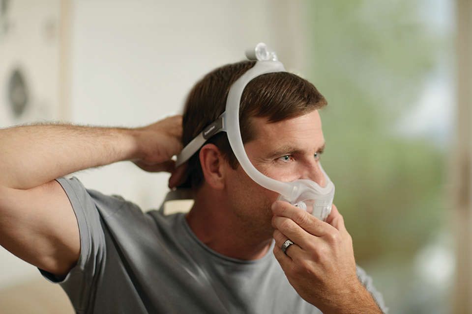 Un uomo regola una maschera facciale completa Philips CPAP DreamWear.