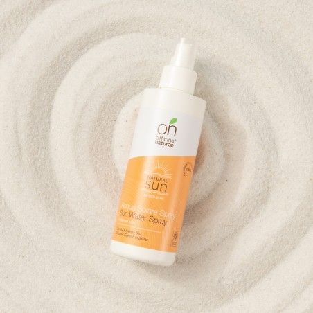 Flacone spray bianco con etichetta arancione su fondo sabbioso. Scritte: Officina Naturae, Natural Sun, Acqua Solare Spray, Sun Water Spray.