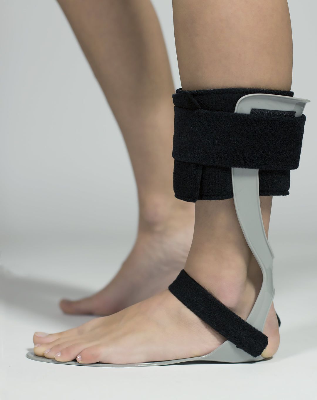 Tutore grigio per caviglia con chiusure in velcro nere, fissato alla gamba di una persona.