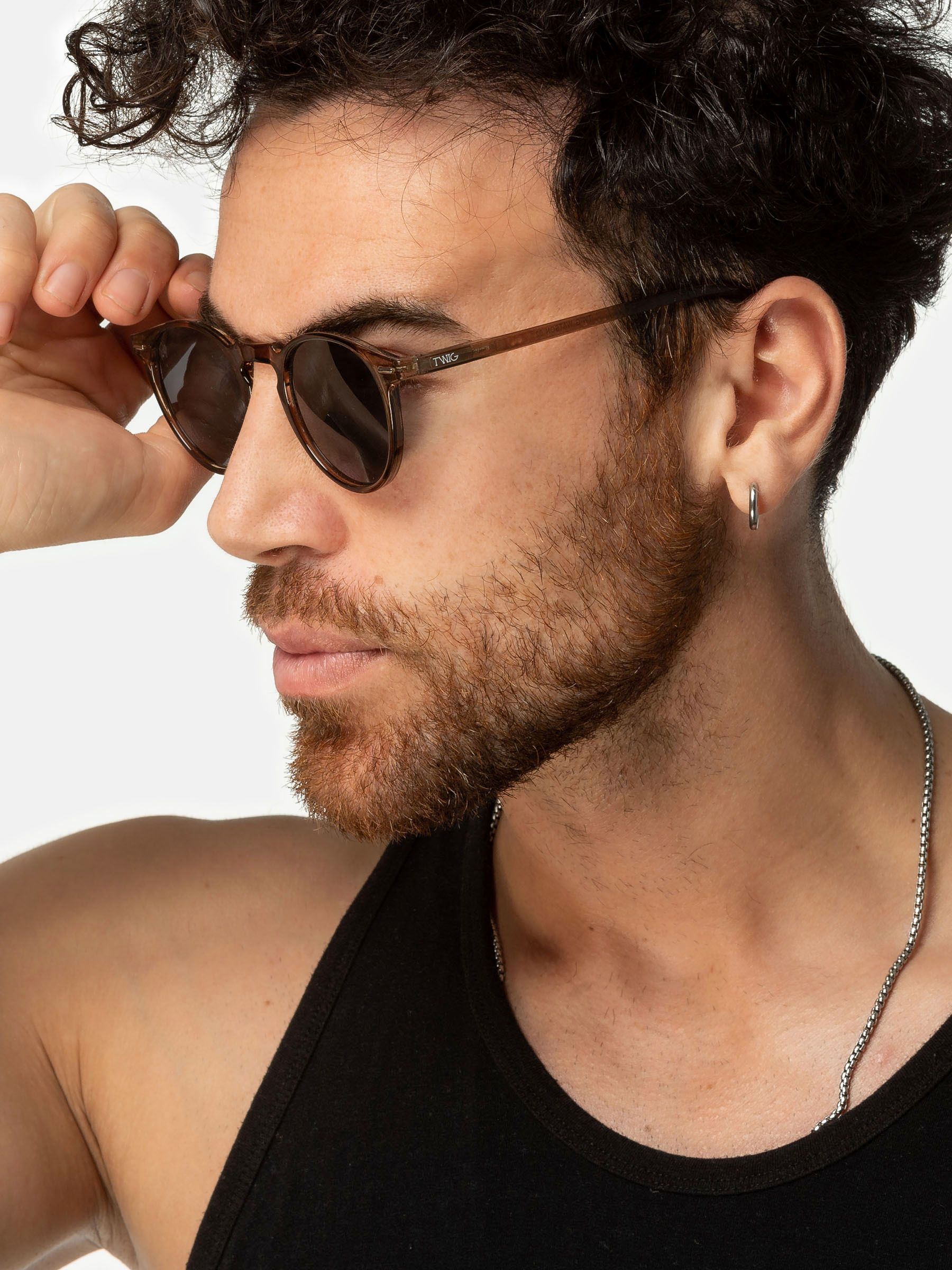 Uomo con occhiali da sole Twig. Montatura marrone, lenti scure, vista laterale.