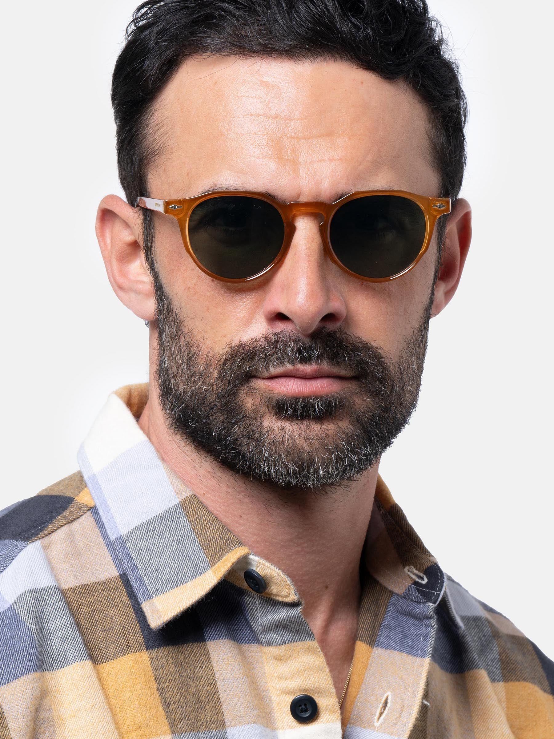 Uomo con occhiali da sole marroni e lenti verdi. Camicia a quadri.