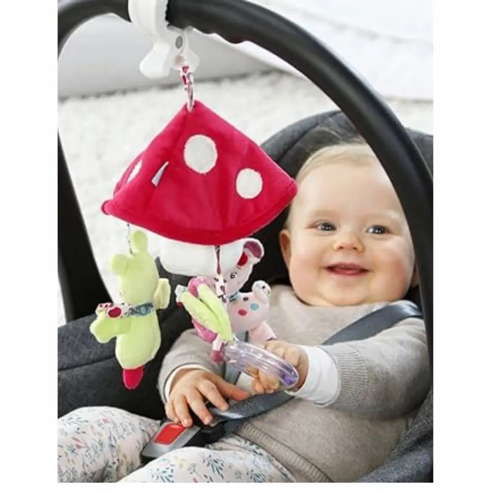 Bambino nel seggiolino auto con mobile. Mobile con fungo, cerbiatto e rana. Bambino sorridente nel seggiolino auto.