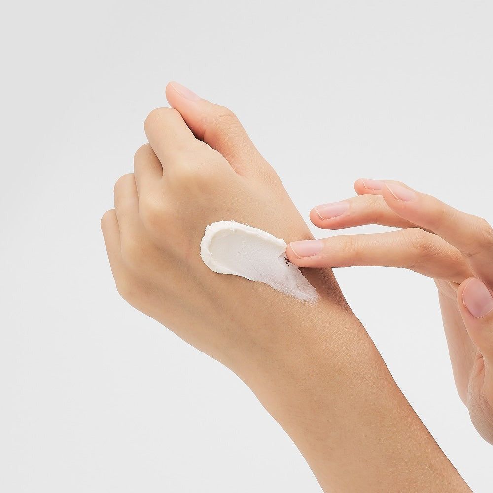 Una mano applica una crema bianca sull'avambraccio.