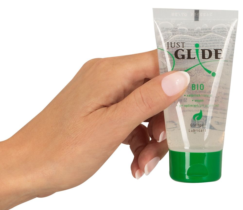 Una mano tiene un tubo di lubrificante con tappo verde. Scritta: Just Glide Bio. Vegano e pH ottimizzato.
