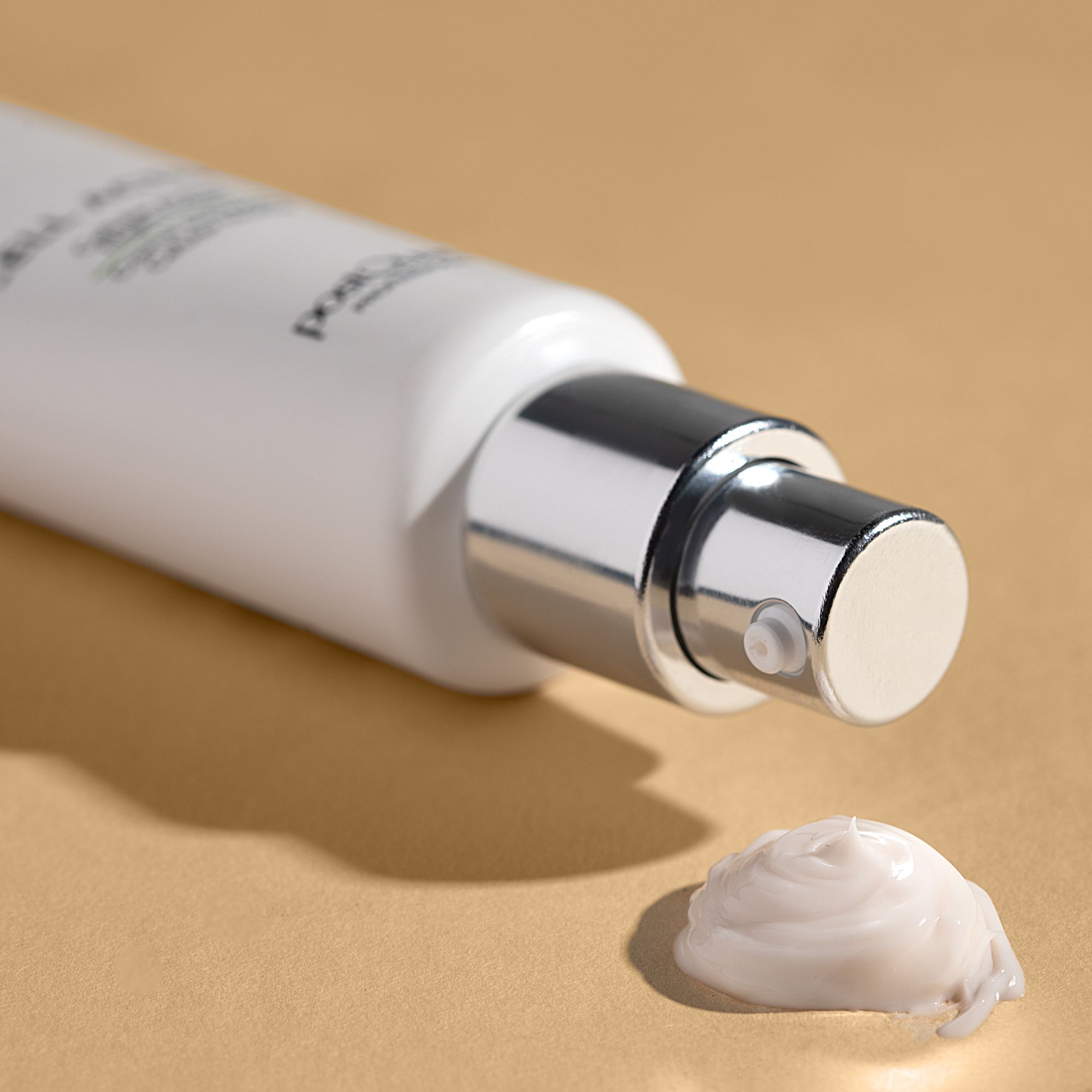 Primo piano di un tubo bianco con chiusura argentata. Crema che esce dall'apertura. Sfondo beige.