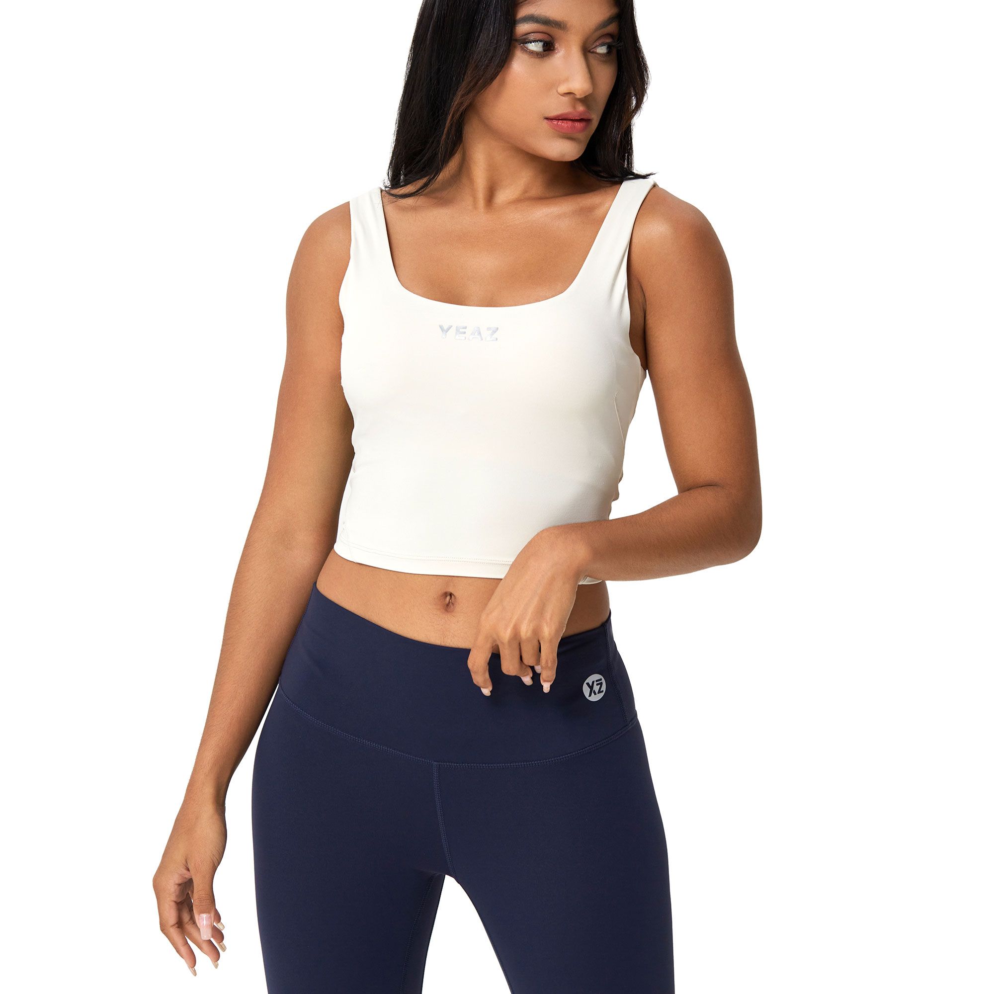 Donna con crop top bianco scollatura quadrata e leggings blu scuro. Logo visibile sul top e sui leggings.
