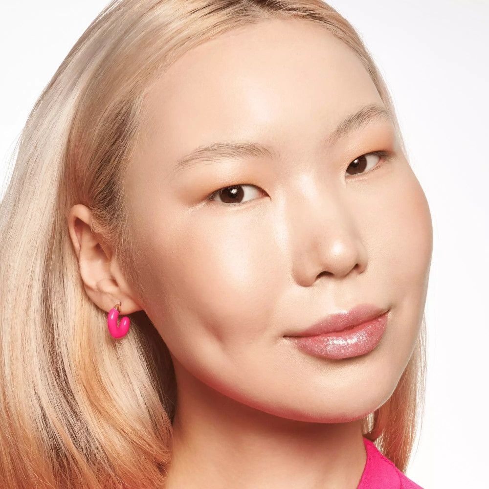 Primo piano di una donna truccata. Indossa orecchini rosa e rossetto. Carnagione chiara.