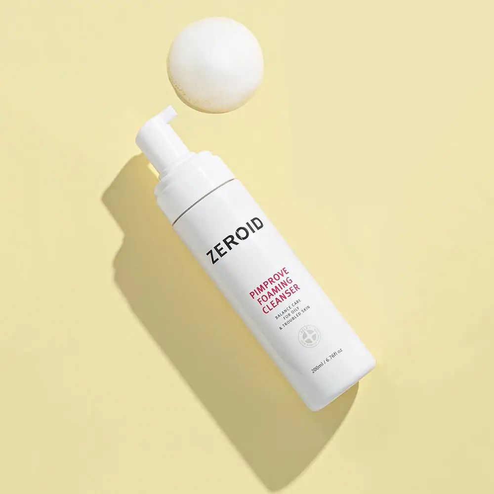 Flacone bianco ZEROID Pimprove Foaming Cleanser con pompa. Nome prodotto e testo. Su sfondo giallo. Sfera di schiuma.
